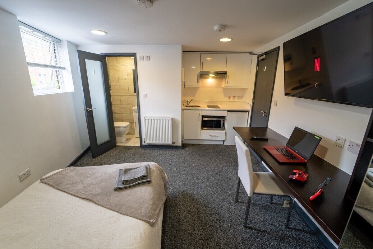 Une chambre d’hôtel compacte comprenant un lit, un bureau avec un ordinateur portable, une télévision et une kitchenette.