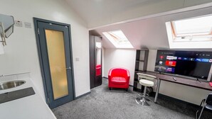 Une chambre d’hôtel avec une kitchenette, un fauteuil rouge, un téléviseur avec accès aux services de diffusion en continu et une fenêtre de toit.