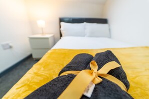 A neatly made bed with a yellow bedspread and two towels tied with a yellow ribbon. - 100 Dale Road Studios in Guest House (Birmingham)