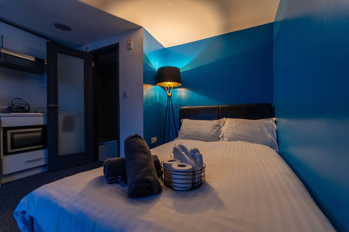 Une chambre d’hôtel avec un lit, une lampe de chevet, une serviette et un panier contenant des articles de toilette.