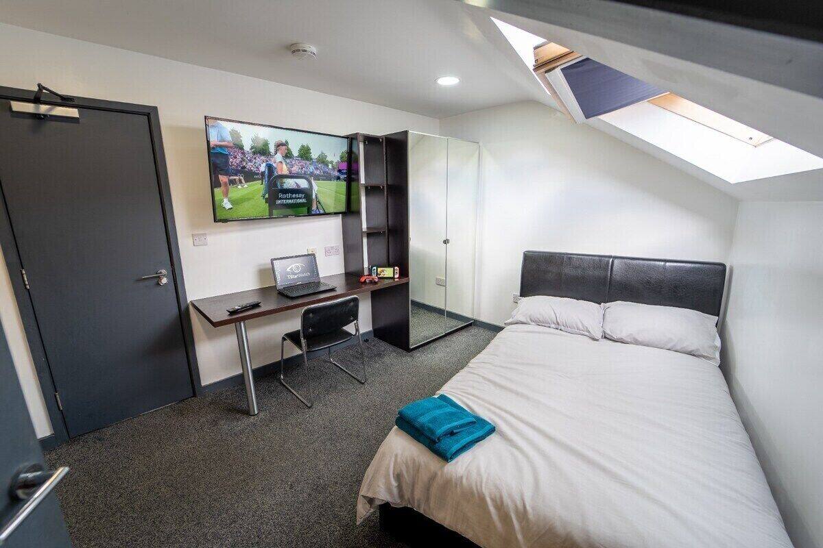 Une chambre d’hôtel équipée d’un lit, d’un bureau avec un ordinateur portable, d’un téléviseur fixé au mur et d’une lucarne.