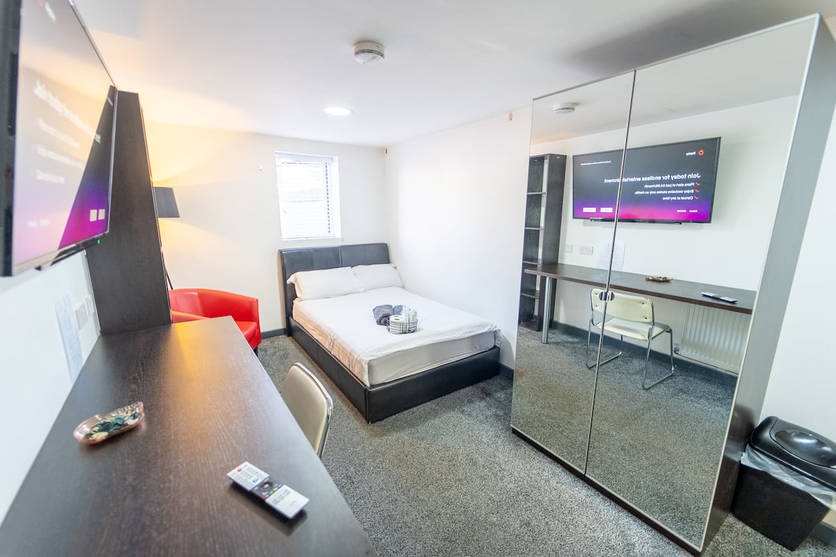 Une chambre d’hôtel moderne équipée d’un lit, d’un bureau, d’une chaise, d’une télévision et d’une cloison en verre.