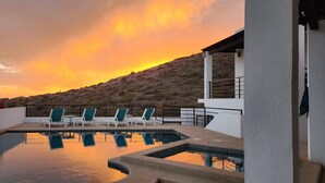 A pool area with lounge chairs and a view of the ocean at sunset.