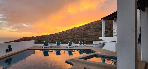 A pool area with lounge chairs and a view of the ocean at sunset.
