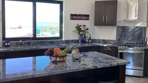 A kitchen with a large window, granite countertops, a stainless steel stove, and a decorative vase with flowers.