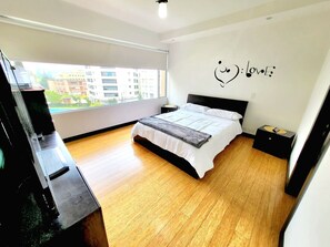 Un dormitorio moderno con una cama grande, una mesita de noche, un aparador y una ventana con vista a la ciudad.