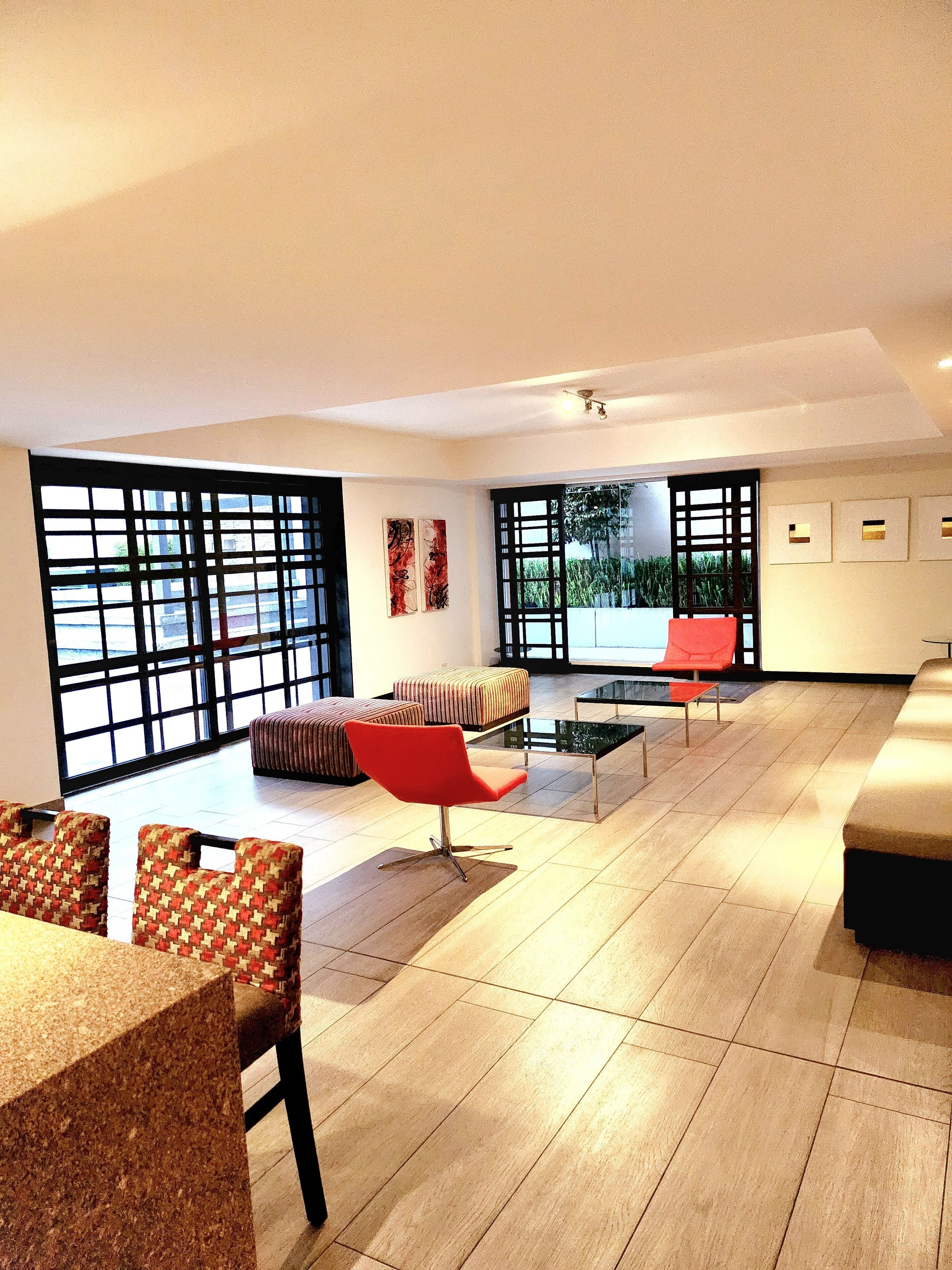 Un vaste espace de vie doté d’une grande fenêtre, d’un fauteuil rouge, d’un canapé et d’une table à manger avec des chaises.