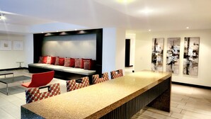 A modern kitchen with a long counter, a seating area with patterned cushions, and abstract wall art.