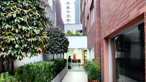 A narrow, paved walkway flanked by lush greenery and red brick buildings.