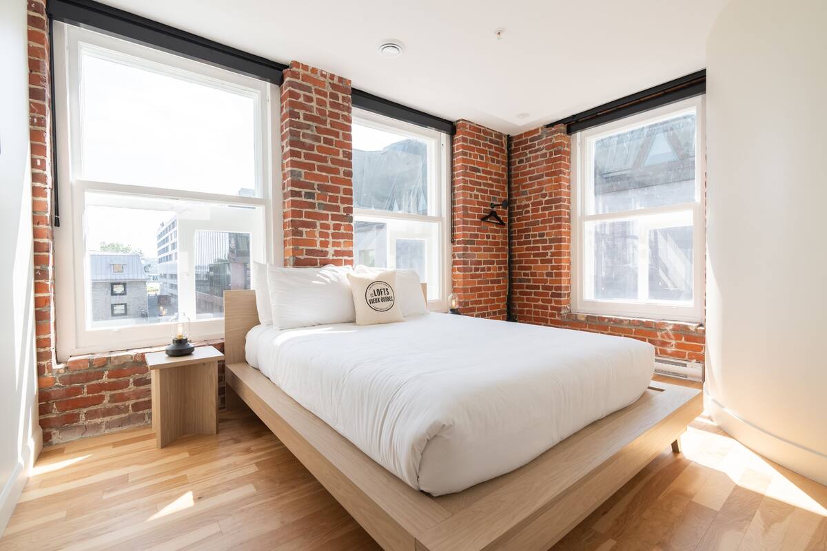 Une chambre moderne avec un lit en mezzanine, des murs en briques, de grandes fenêtres et un plancher en bois.