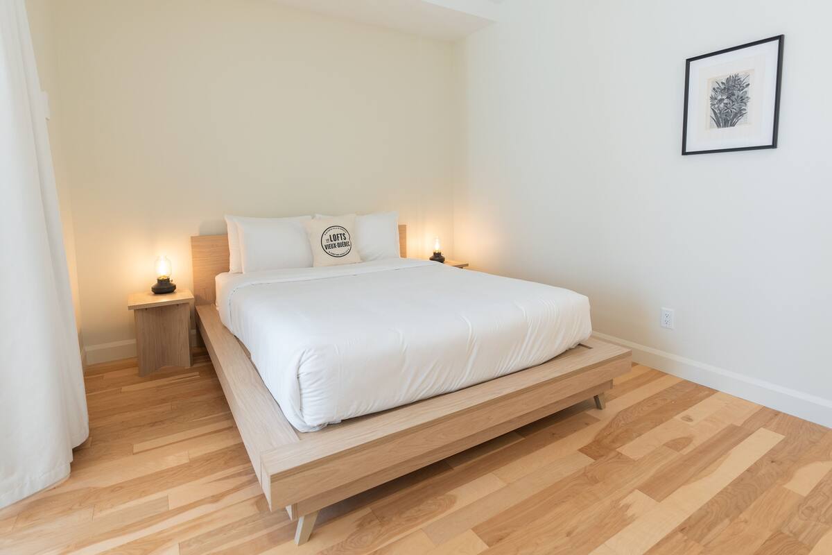 Une chambre à coucher au style minimaliste, avec un lit, des tables de chevet et un tableau encadré au mur.