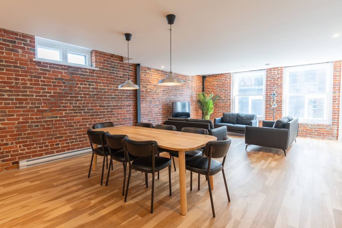 Un salon moderne avec un mur en briques, une table à manger en bois avec des chaises, un canapé noir et un téléviseur.