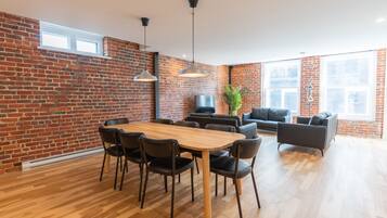 A modern living room with a brick wall, a wooden dining table with chairs, a black sofa, and a TV.