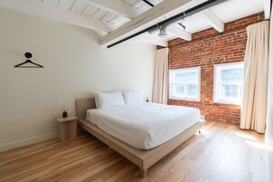 Un dormitorio con cama de madera, pared de ladrillo y ventana con cortinas.