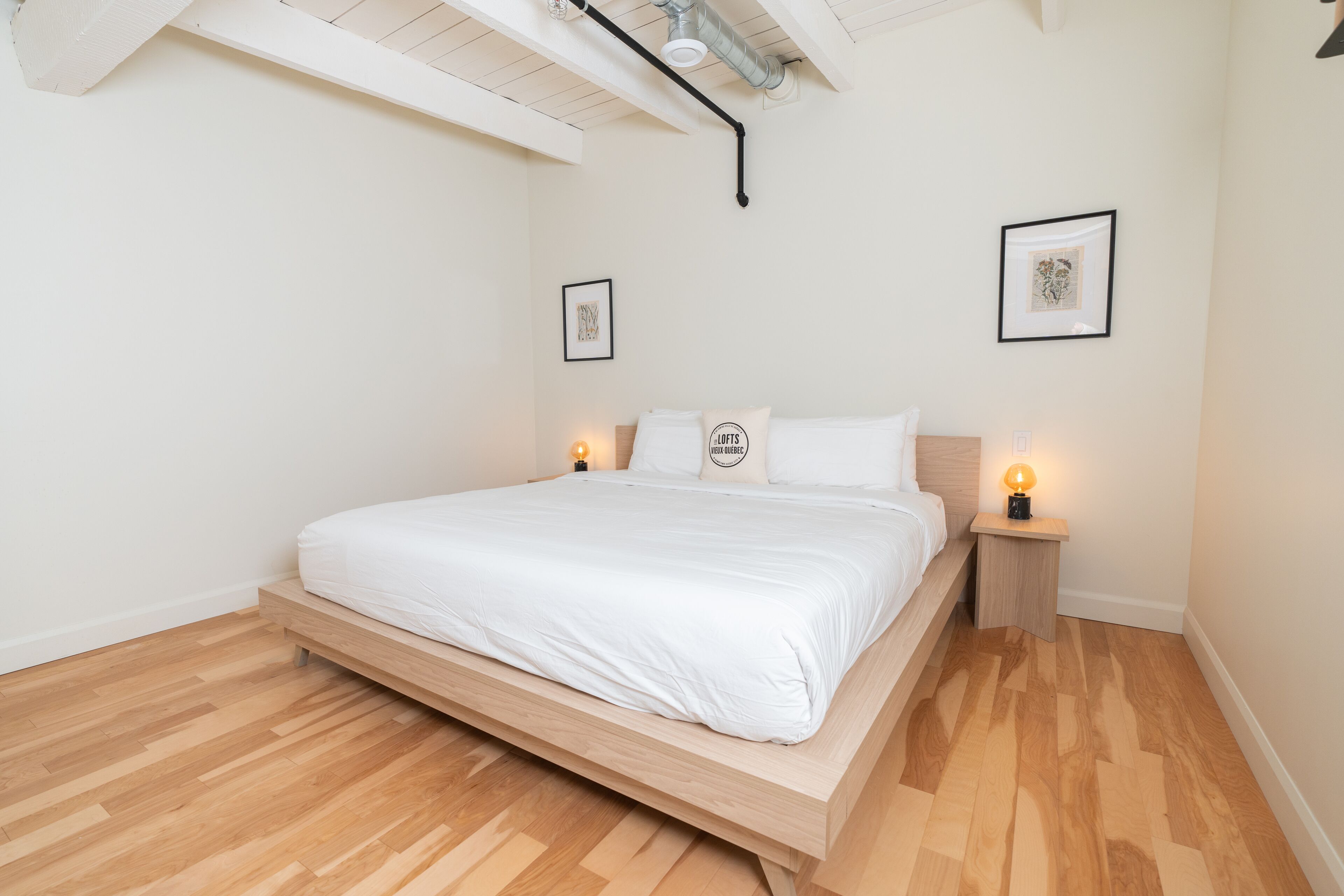 Quarto minimalista com estrutura de cama de madeira, roupa de cama branca e duas luminárias de cabeceira.