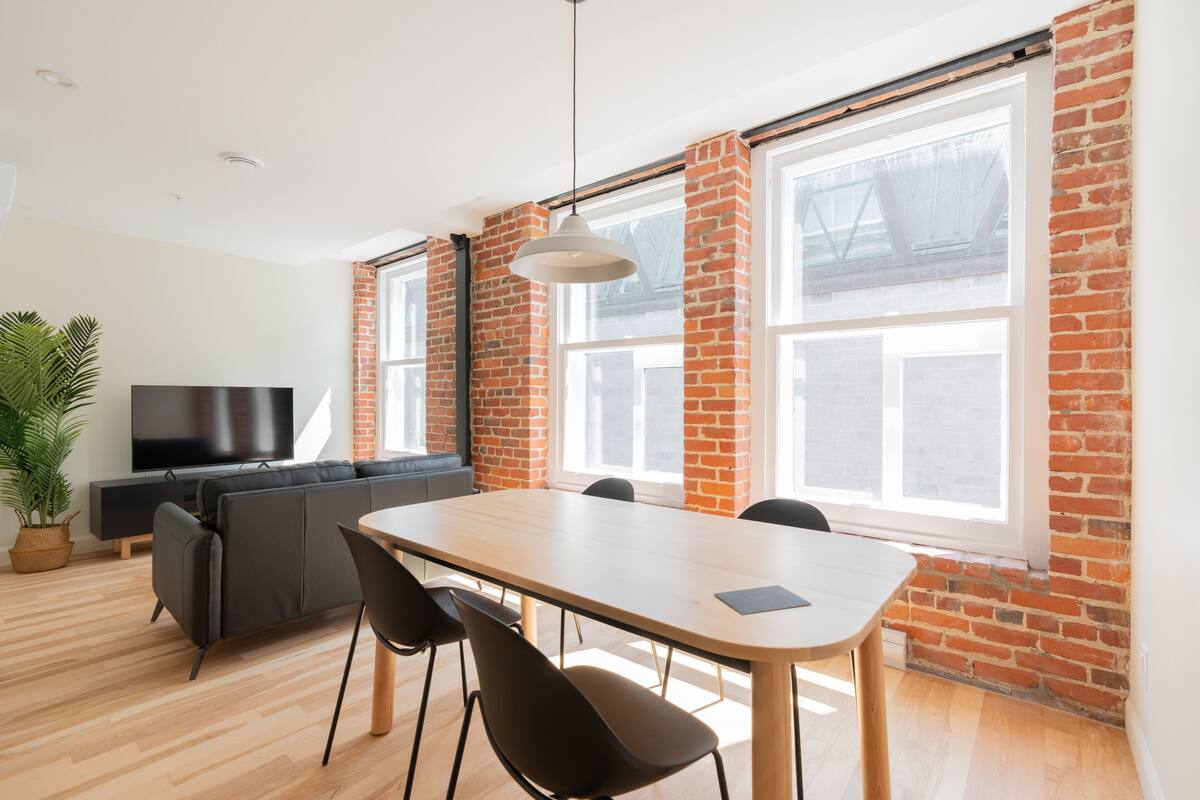 Un salon moderne avec une table à manger, un canapé noir et un téléviseur.