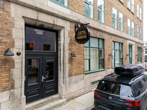 Un immeuble avec une porte et des fenêtres noires, une enseigne indiquant « LOFTS DE LA BARRICADE » et une voiture garée.