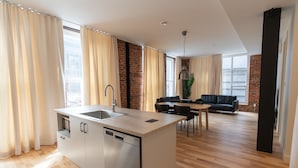 Eine moderne Küche mit Geschirrspüler, eine Essecke mit Tisch und Stühlen sowie ein Wohnzimmer mit Sofa.