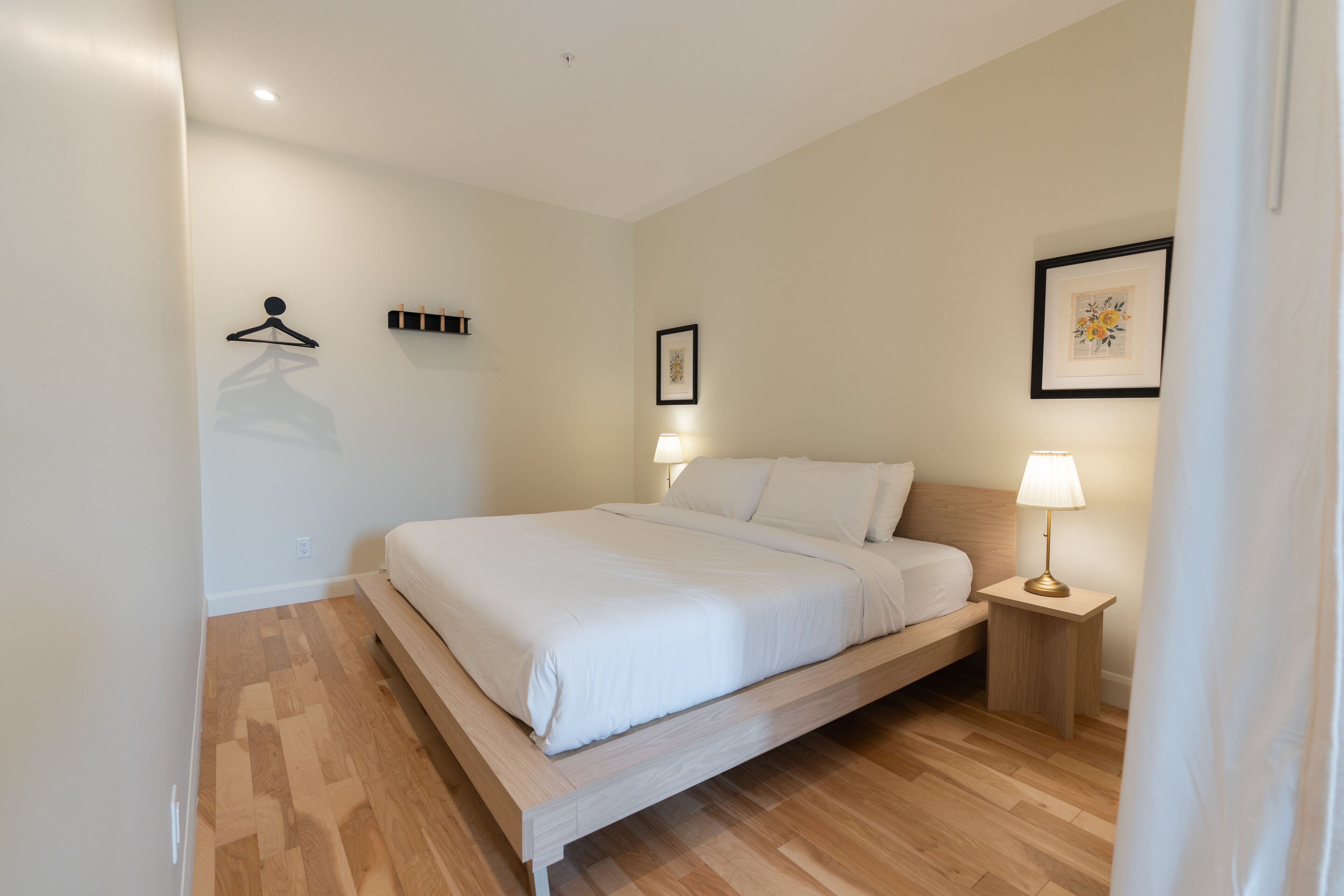 A bedroom with a bed, bedside tables, a wall-mounted hanger, and a framed picture.