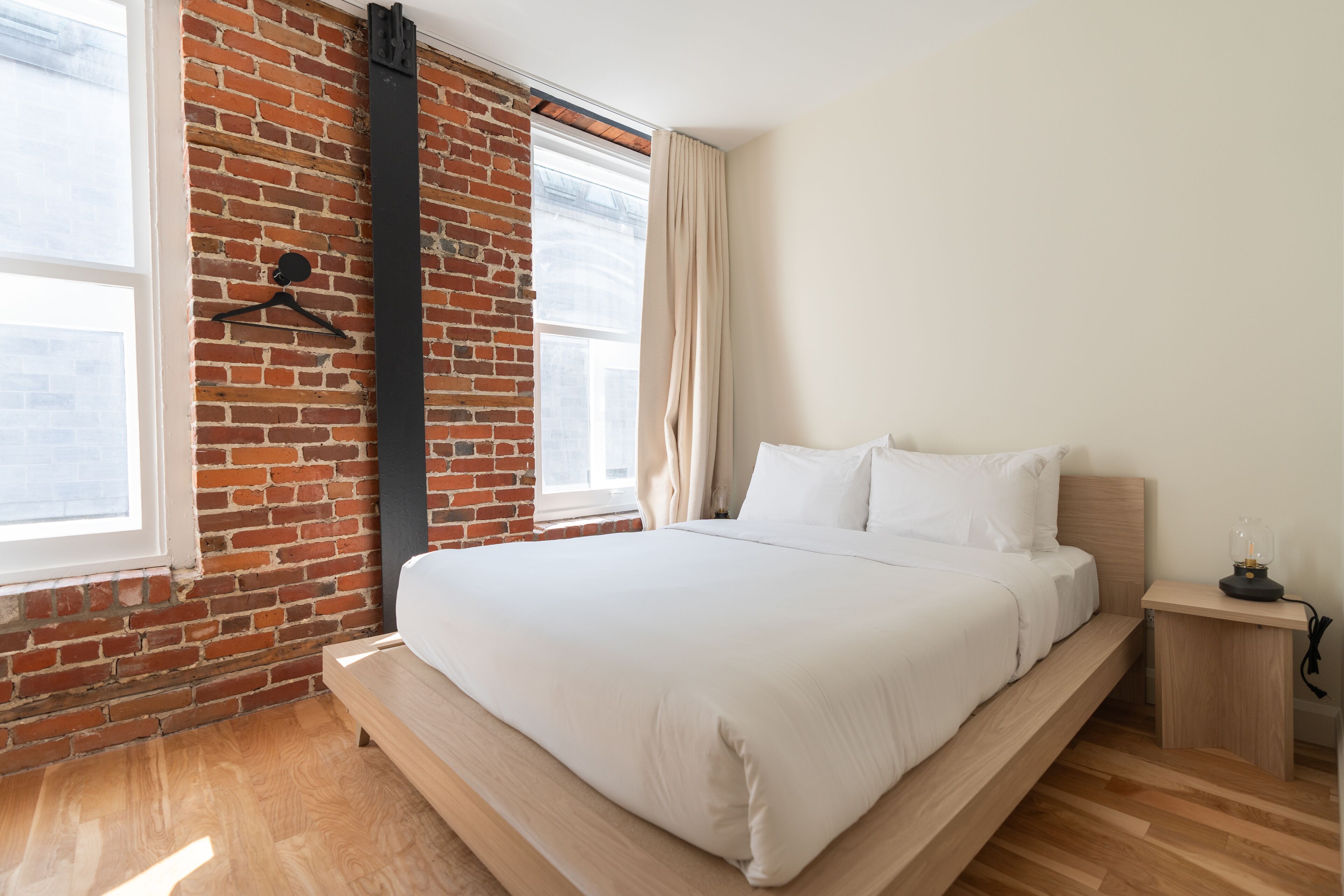 Un dormitorio moderno con pared de ladrillo, estructura de cama de madera y una pequeña mesita de noche.