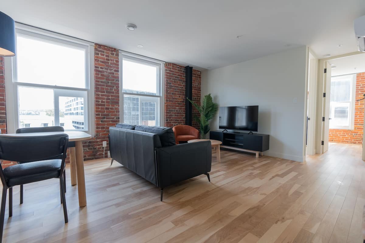 Un salon moderne avec un canapé, des fauteuils, un téléviseur et un mur en briques.