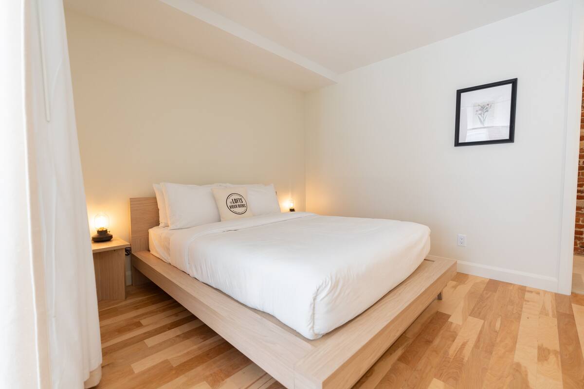 Une chambre à coucher moderne avec un lit surélevé en bois, une table de chevet avec une lampe et un tableau encadré au mur.