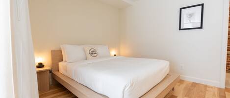 A modern bedroom with a wooden platform bed, a nightstand with a lamp, and a framed picture on the wall.