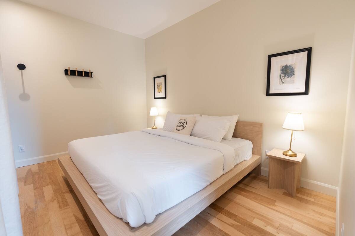 Une chambre à coucher bien rangée, avec un lit simple, des tables de chevet et des lampes fixées au mur.