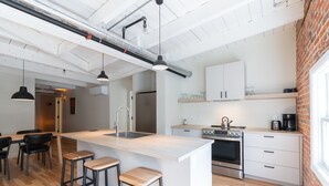 Eine moderne Küche mit Kochinsel, Barhocker, Edelstahlgeräten und einer Wand mit Ziegeloptik.