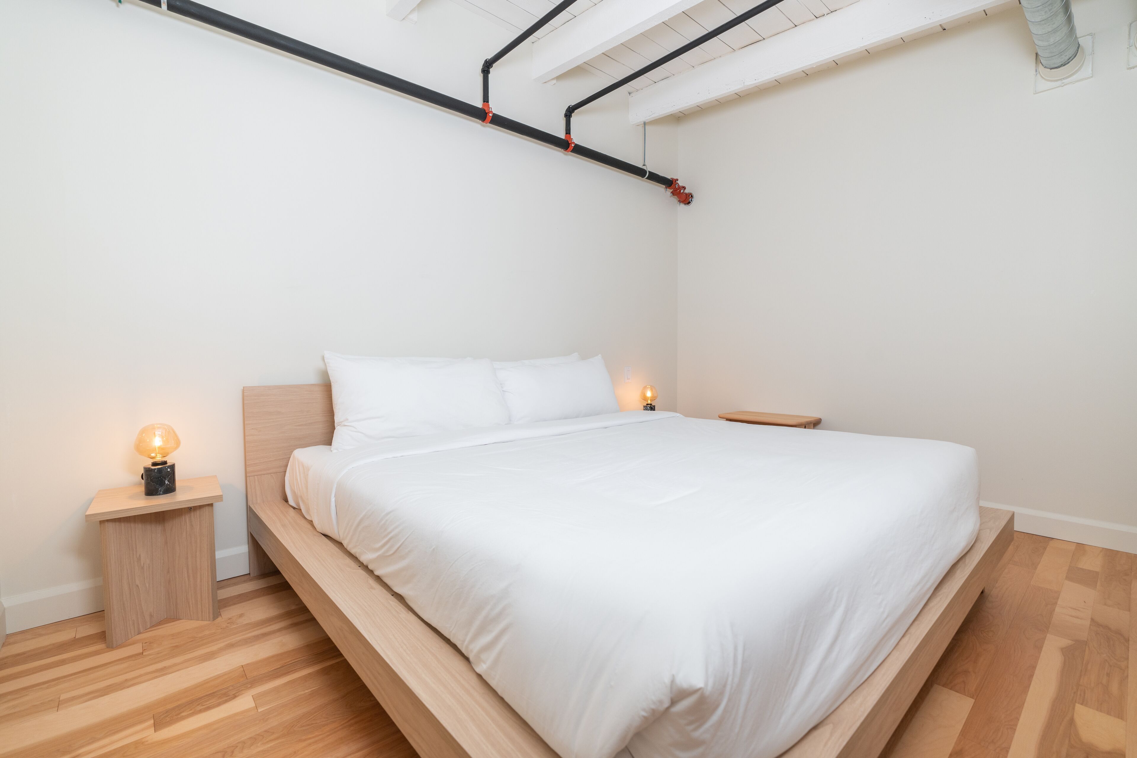 A minimalist bedroom with a wooden bed, white bedding, and two bedside lamps.