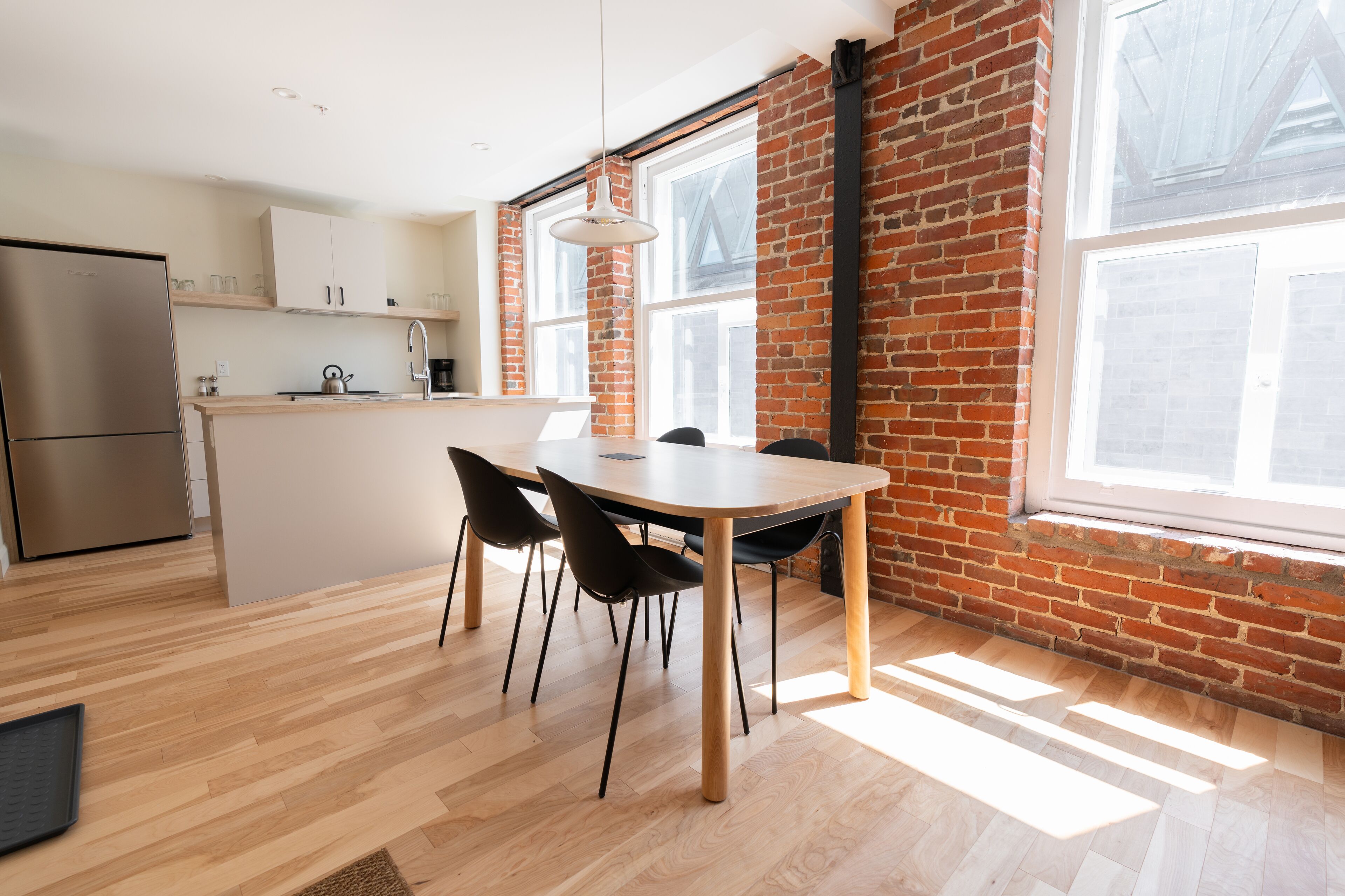 A modern kitchen with a large island, wooden flooring, and a brick wall.
