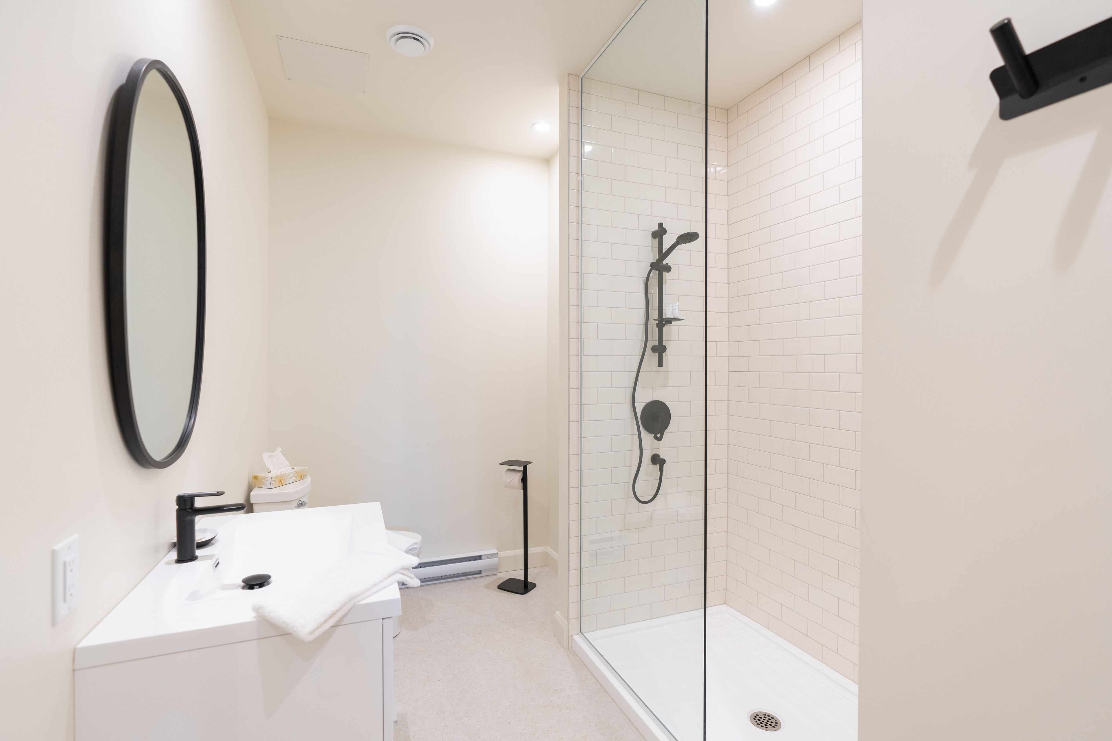 Une salle de bain moderne avec un lavabo blanc, un robinet noir et une douche séparée par une paroi de verre.