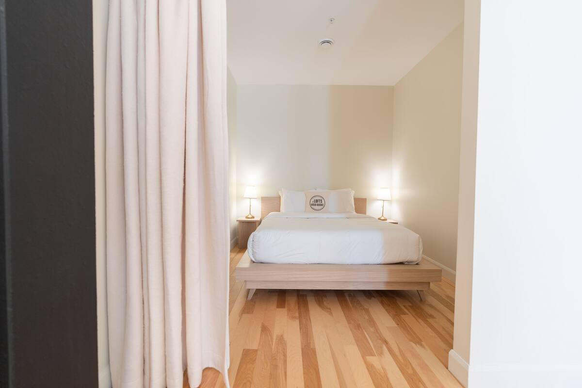 Une chambre d’hôtel avec un plancher en bois, un lit avec une literie blanche, deux lampes de chevet et une table de chevet.