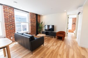 Una sala moderna con una pared de ladrillo decorativa, un televisor de pantalla plana, un sofá, una mesa de comedor y piso de madera.