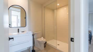 Et moderne badeværelse med et hvidt underskab, toilet og brusekabine med glasvægge.