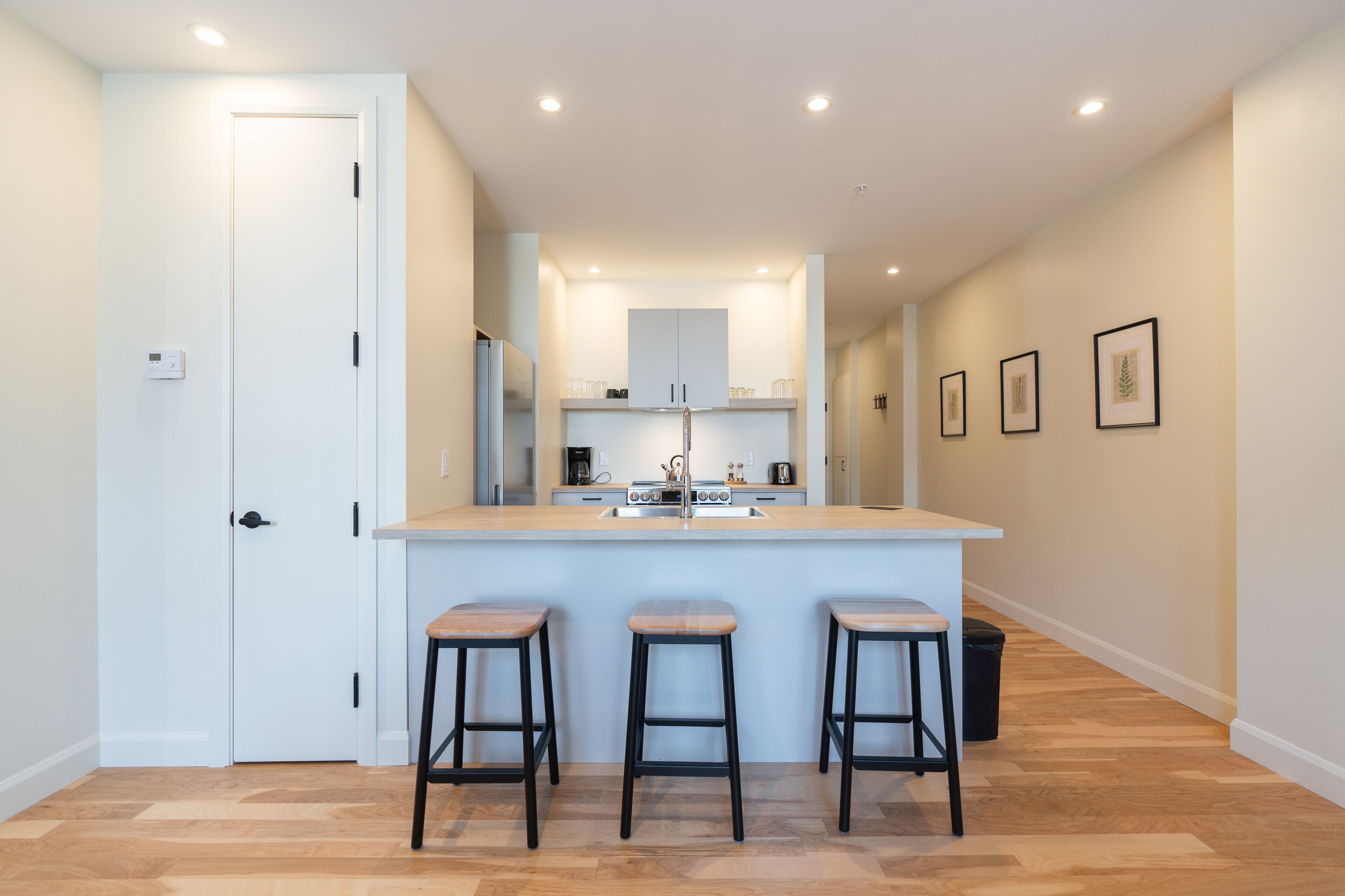A modern kitchen with a central island, three stools, and a door on the left.