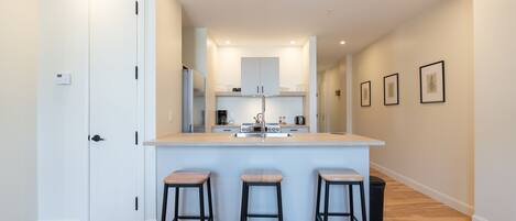 A modern kitchen with a central island, three stools, and a door on the left.