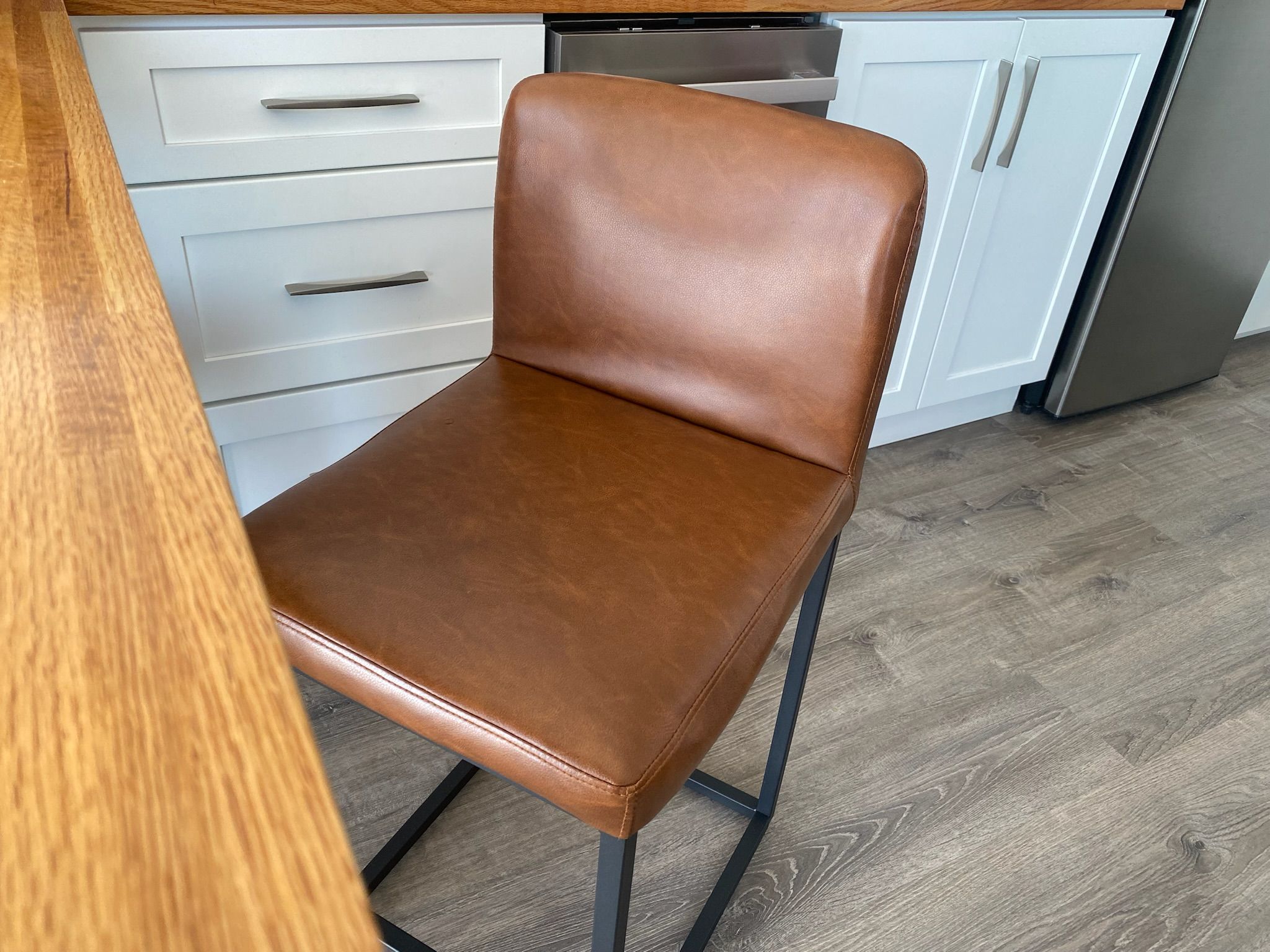 A kitchen with a brown leather chair, white cabinets, and a stainless steel refrigerator.