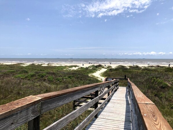A wooden boardwalk leading to a beach with a clear sky.