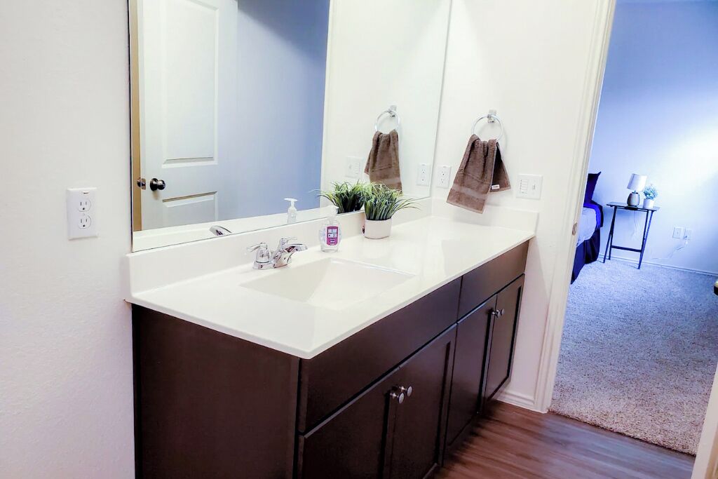 A bathroom with a white sink, dark cabinets, a large mirror, a potted plant, and a towel rack.