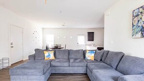 A modern living room with a grey sectional sofa, wooden flooring, and a dining area in the background. - ENTIRE HOME | 3BR WFH Hub | Fast 300 Mbps Wi-Fi | Near SoCo (Austin)