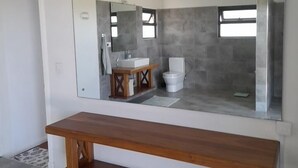 A bathroom with a large mirror, a wooden bench, a sink, and a toilet. - Jags villa (Union Vale)