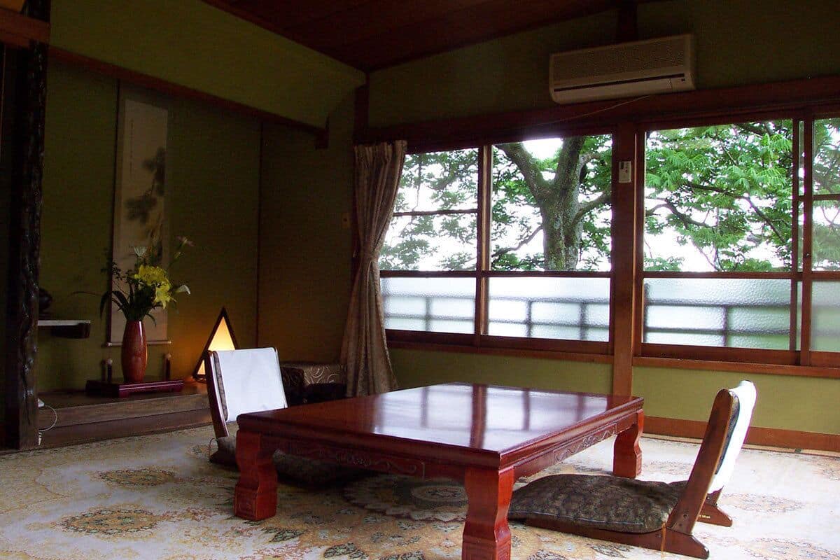 Una habitación tradicional japonesa con suelo de tatami, una mesa de madera baja y vistas al verdor a través de amplios ventanales.