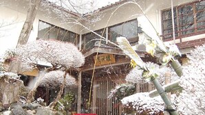 Un edificio japonés tradicional con una puerta de madera, un sendero de piedra y plantas cubiertas de nieve.