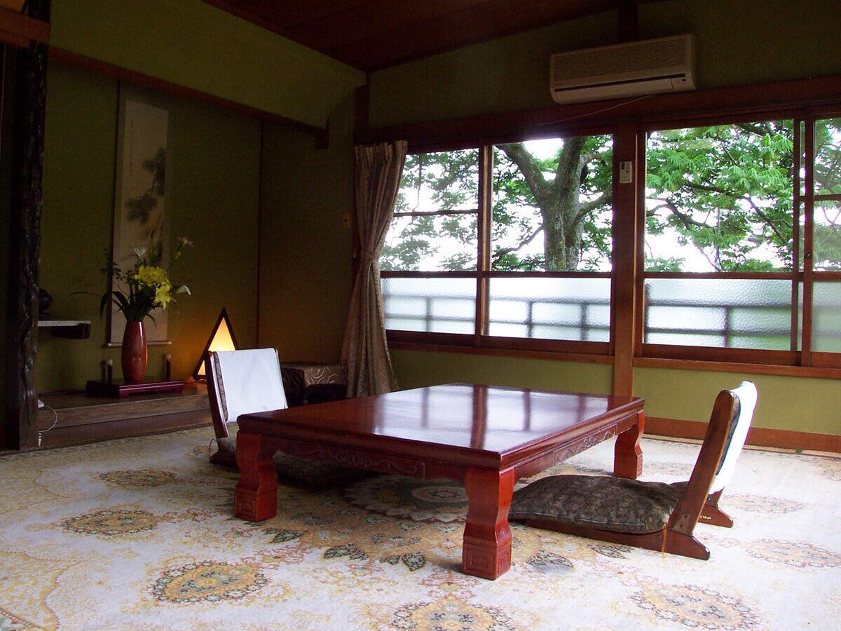 A traditional room with a wooden table, chairs, a lamp, and a large window with a view of trees.