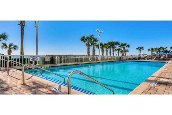 Relax by the pool surrounded by palm trees and a brick-paved area.