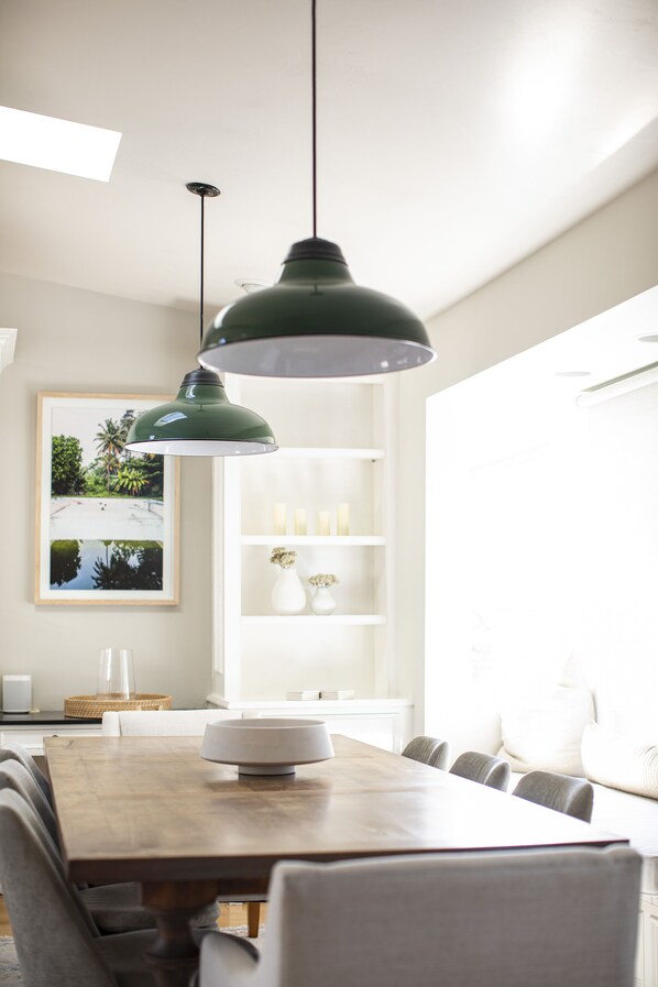 Un coin repas avec une table en bois, des chaises, des lampes suspendues, une étagère blanche ornée de bougies et un tableau encadré accroché au mur.