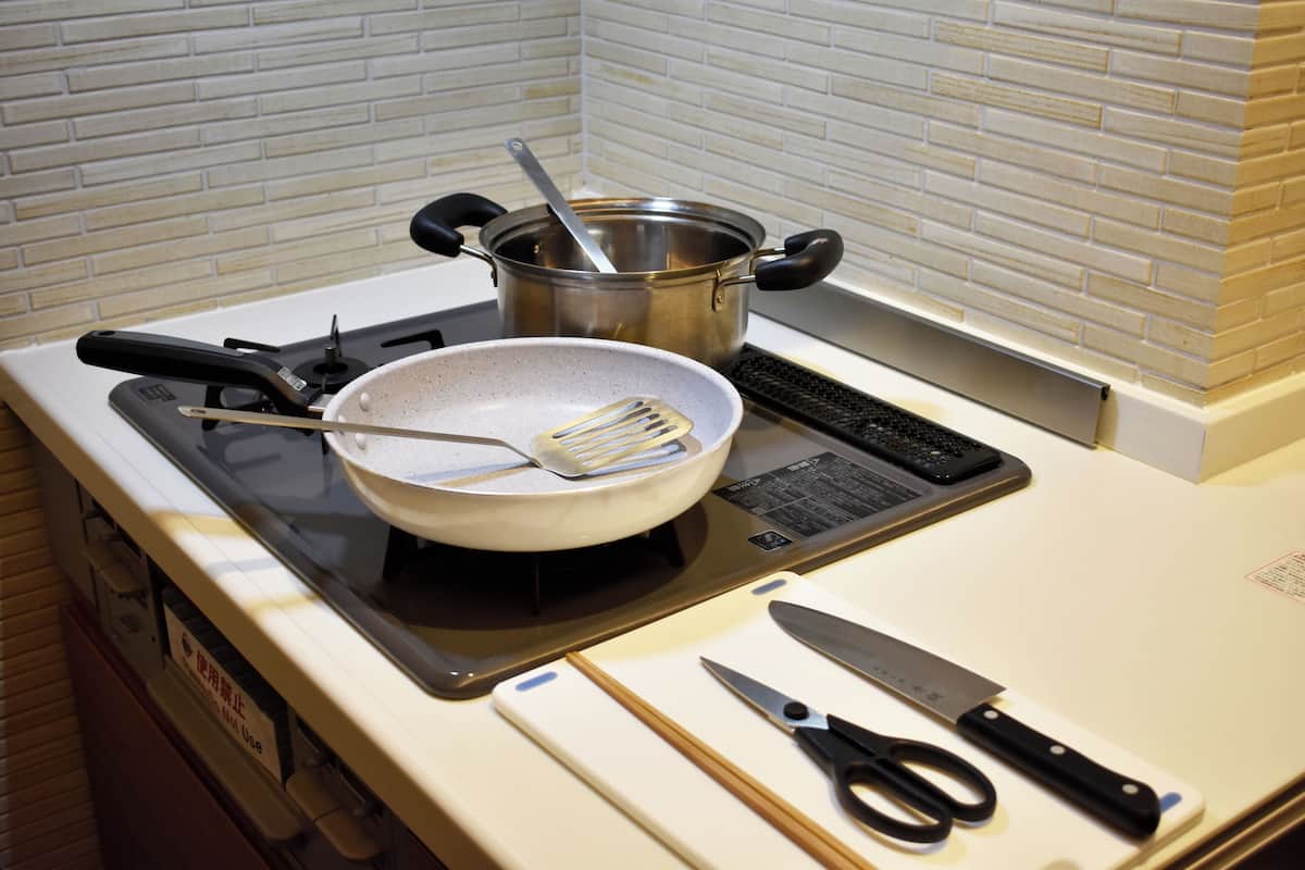 Une cuisine équipée d’une cuisinière, de casseroles, d’une poêle, d’une spatule, d’un couteau et d’une paire de ciseaux posés sur le plan de travail.