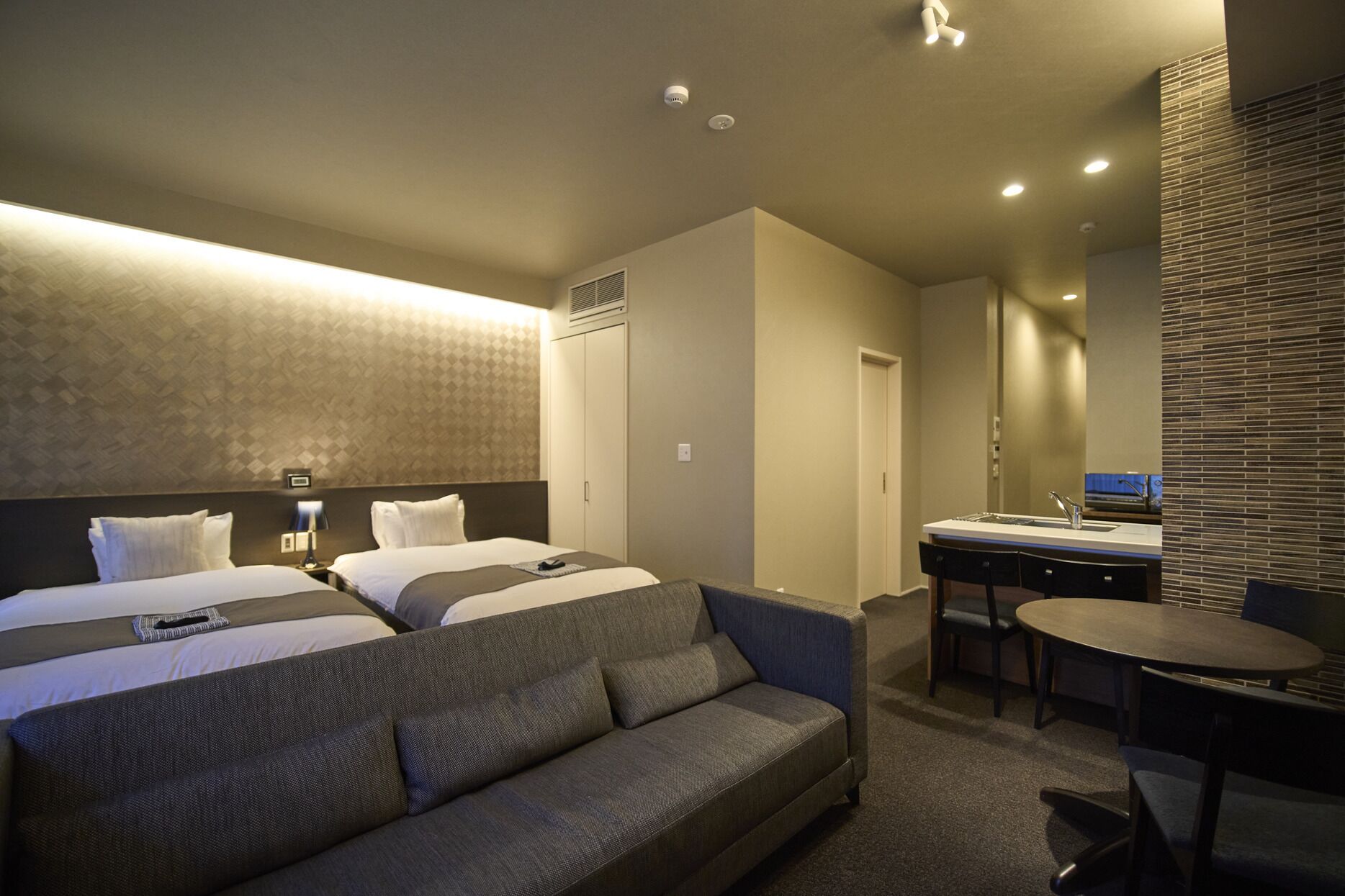 Ein modernes Hotelzimmer mit einem großen Bett, einer Sitzecke, einem Schreibtisch mit Spüle und einem Spiegel.
