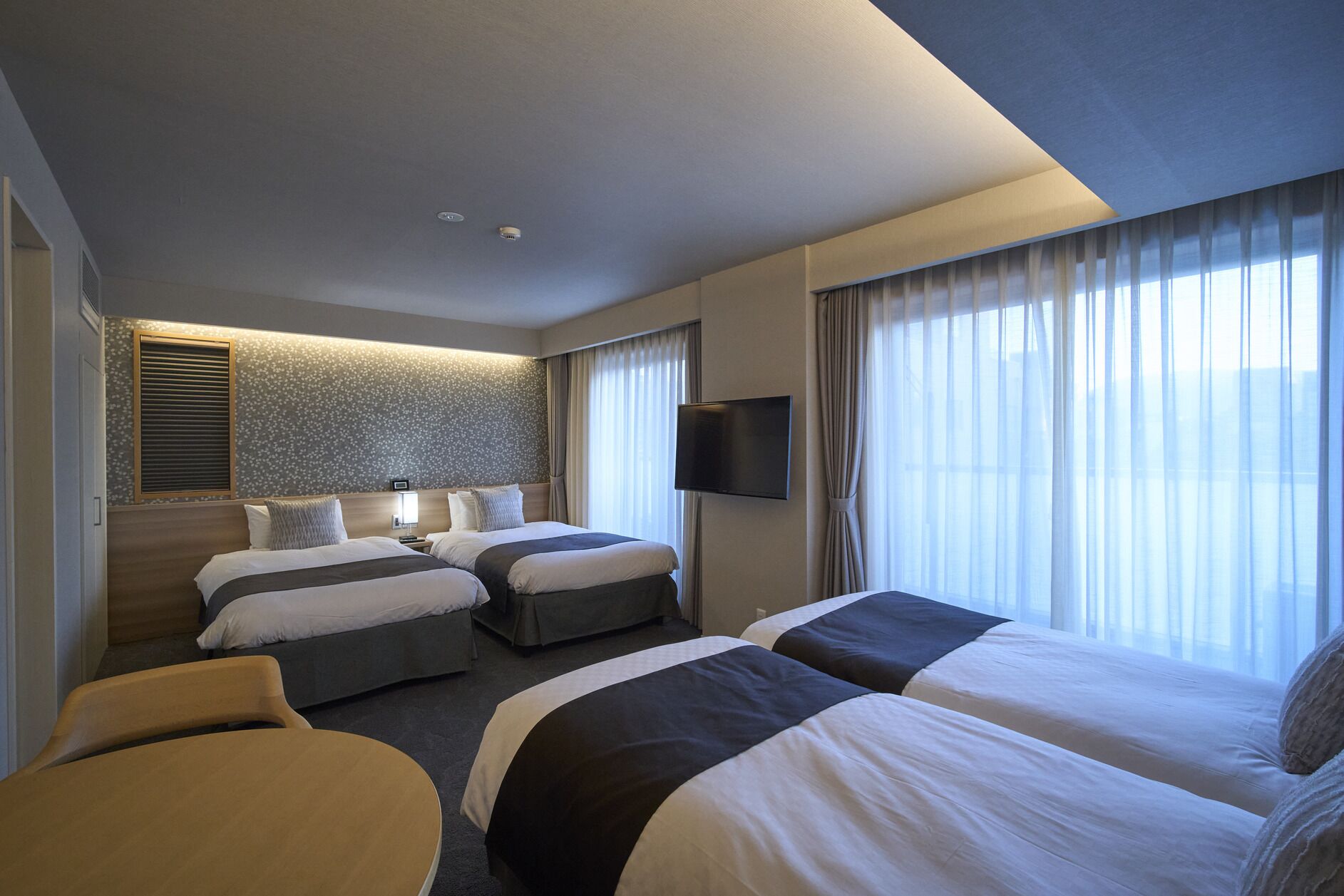 Ein Hotelzimmer mit zwei Betten, einem Fernseher, einem kleinen Tisch und einem Fenster mit Vorhängen.